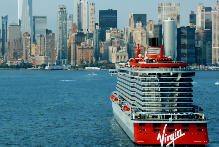 A virgin cruise ship is in the water in front of a city skyline