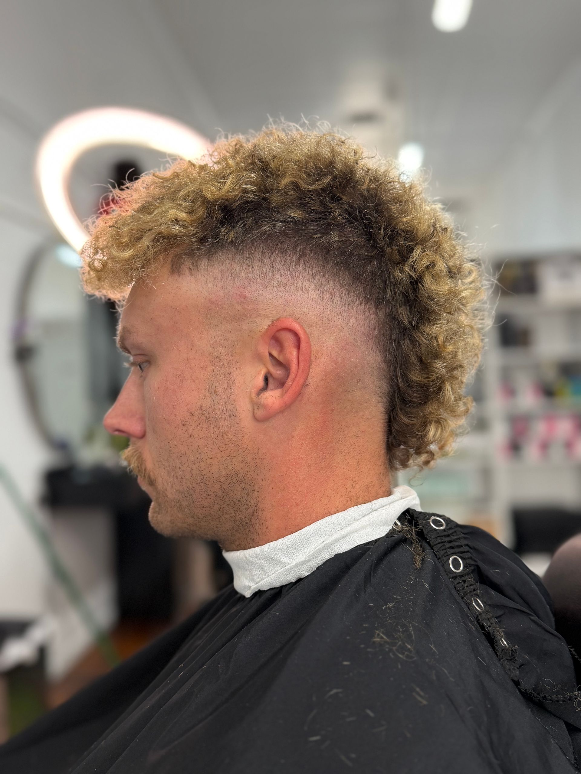 Side profile of a person getting a curly mohawk fade haircut in a salon