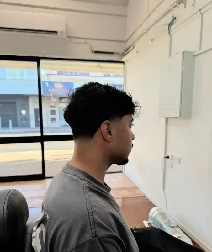 Side profile of a person seated in a bright office, facing a window and white wall. — Ultimate Barber in Maryborough, QLD