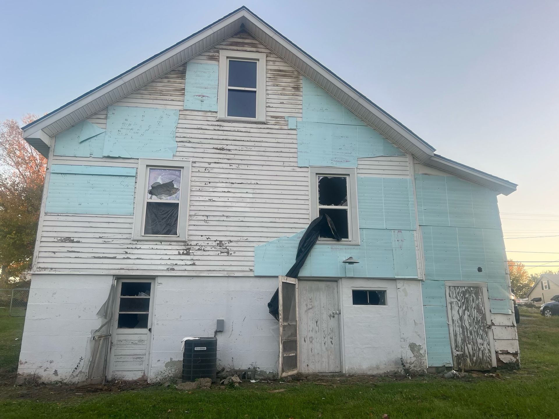 Dilapidated two-story house with peeling white and light blue paint and a sagging front opening