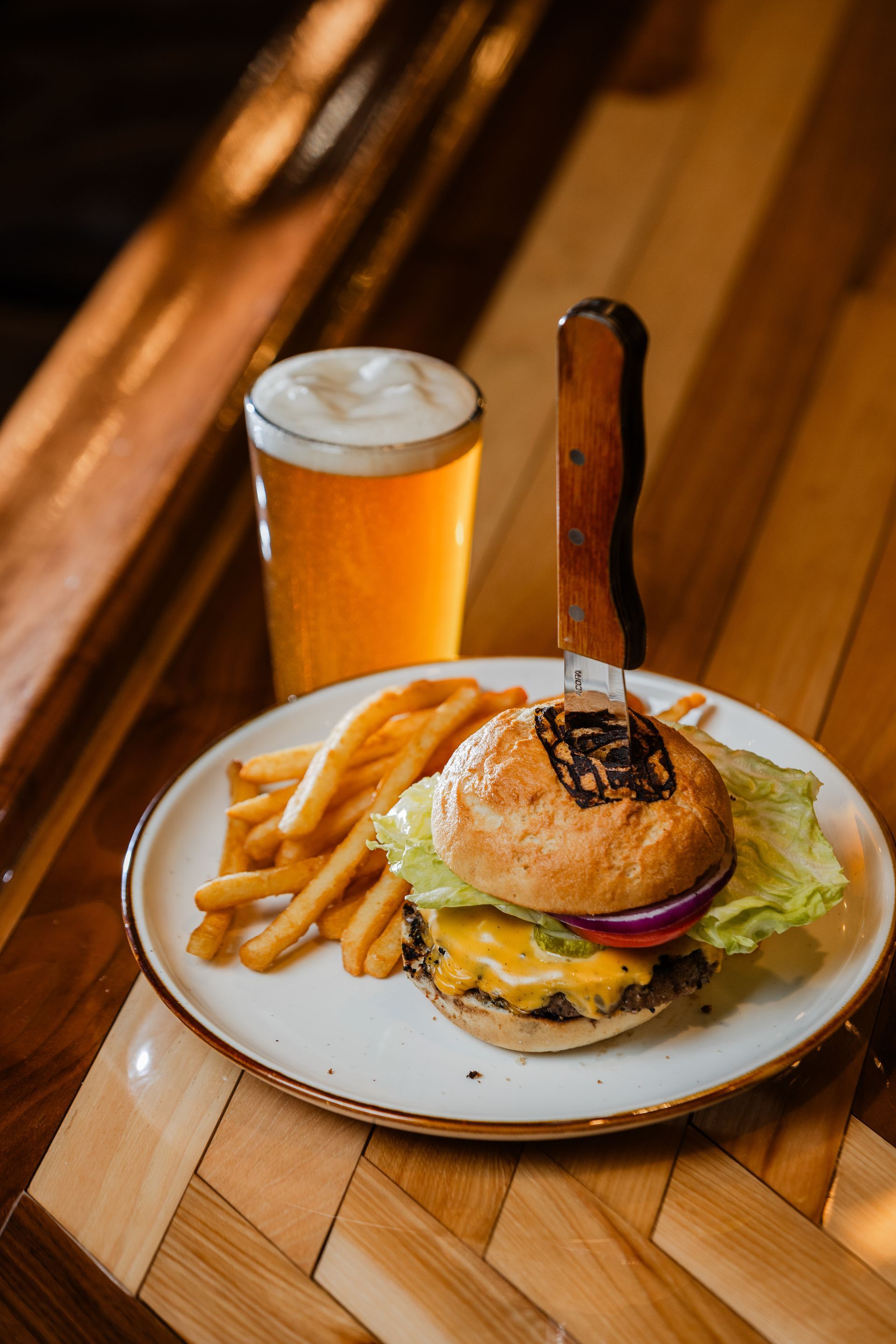 A hamburger and french fries on a plate next to a glass of beer.