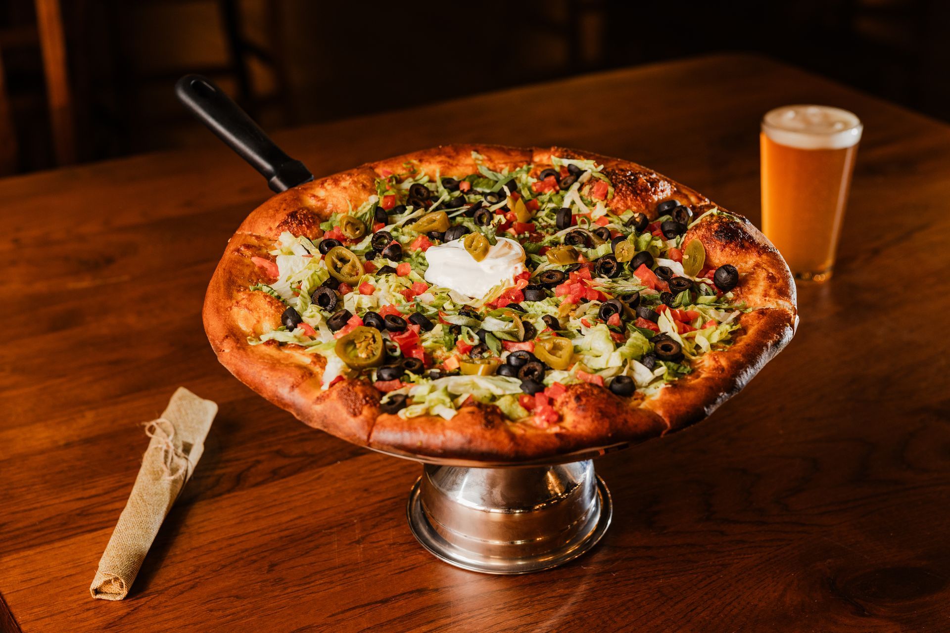 A pizza is sitting on a plate on a table next to a glass of beer.
