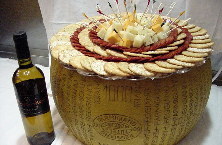 A bottle of wine sits next to a large piece of cheese