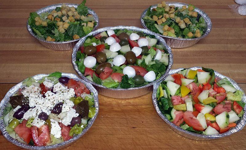 Four aluminum foil containers filled with different types of salads on a wooden table.