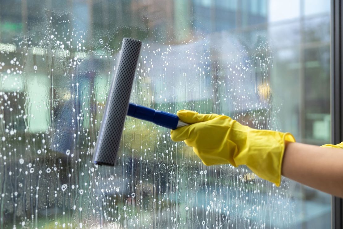 Hand in yellow glove using a squeegee to clean a rain-speckled glass window