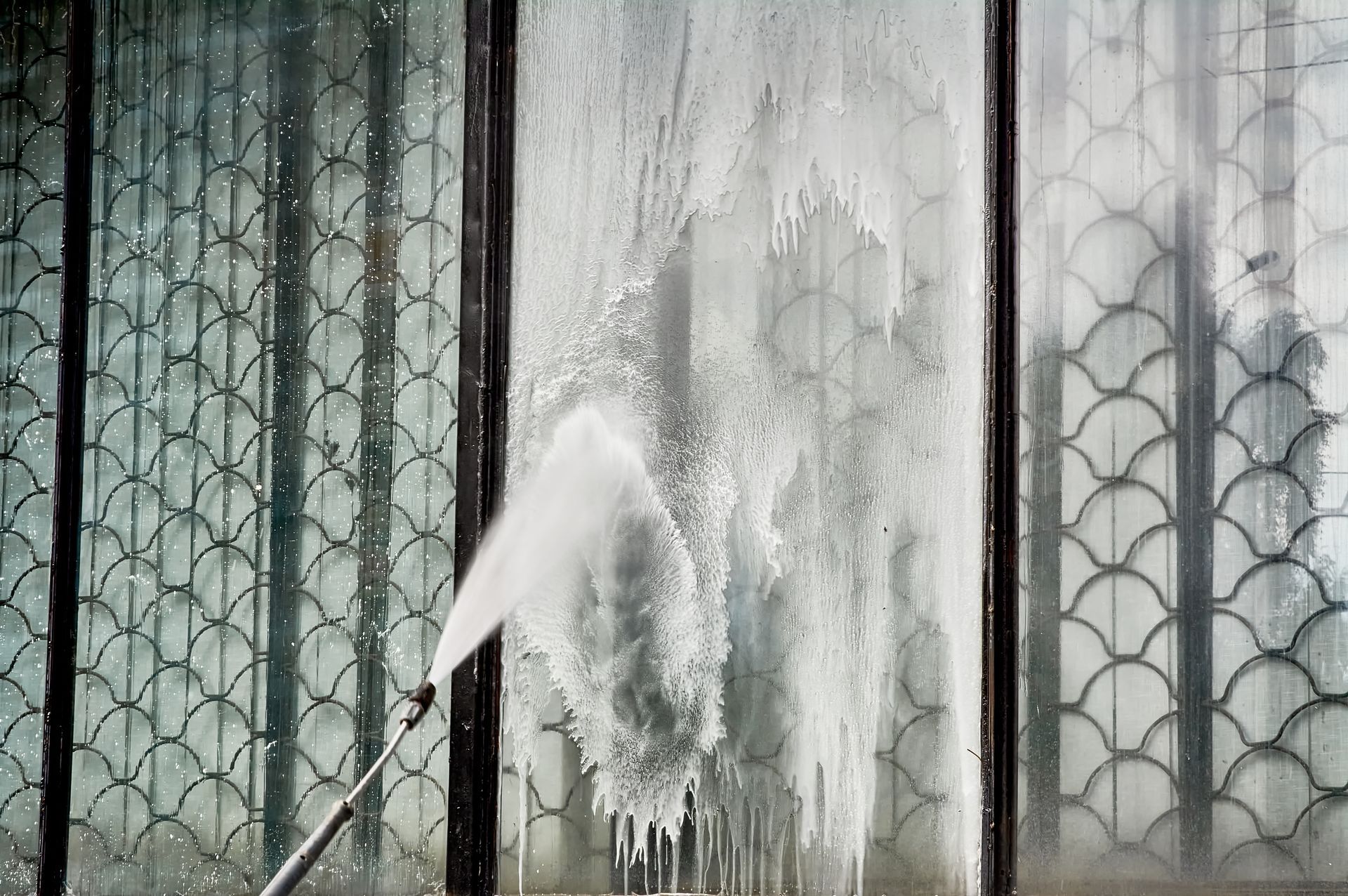 Pressure washer blasting grime off a metal gate, with white spray and cleaning streaks.
