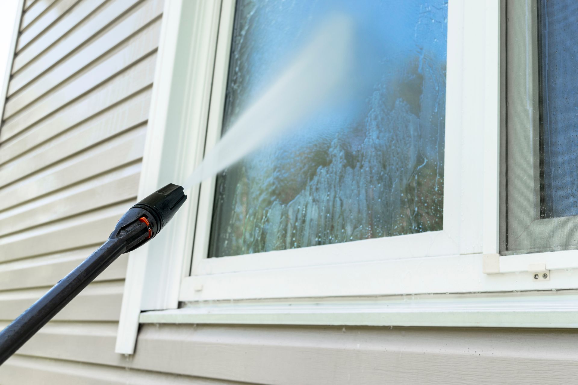 Pressure washer spraying a house window and siding with water