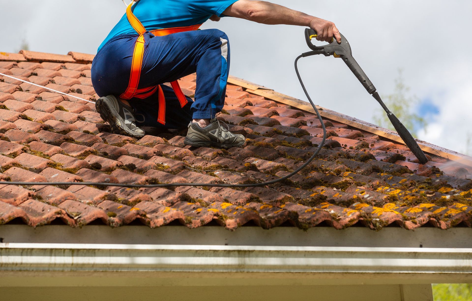 Worker pressure-washing a red tile roof with a hose and wand