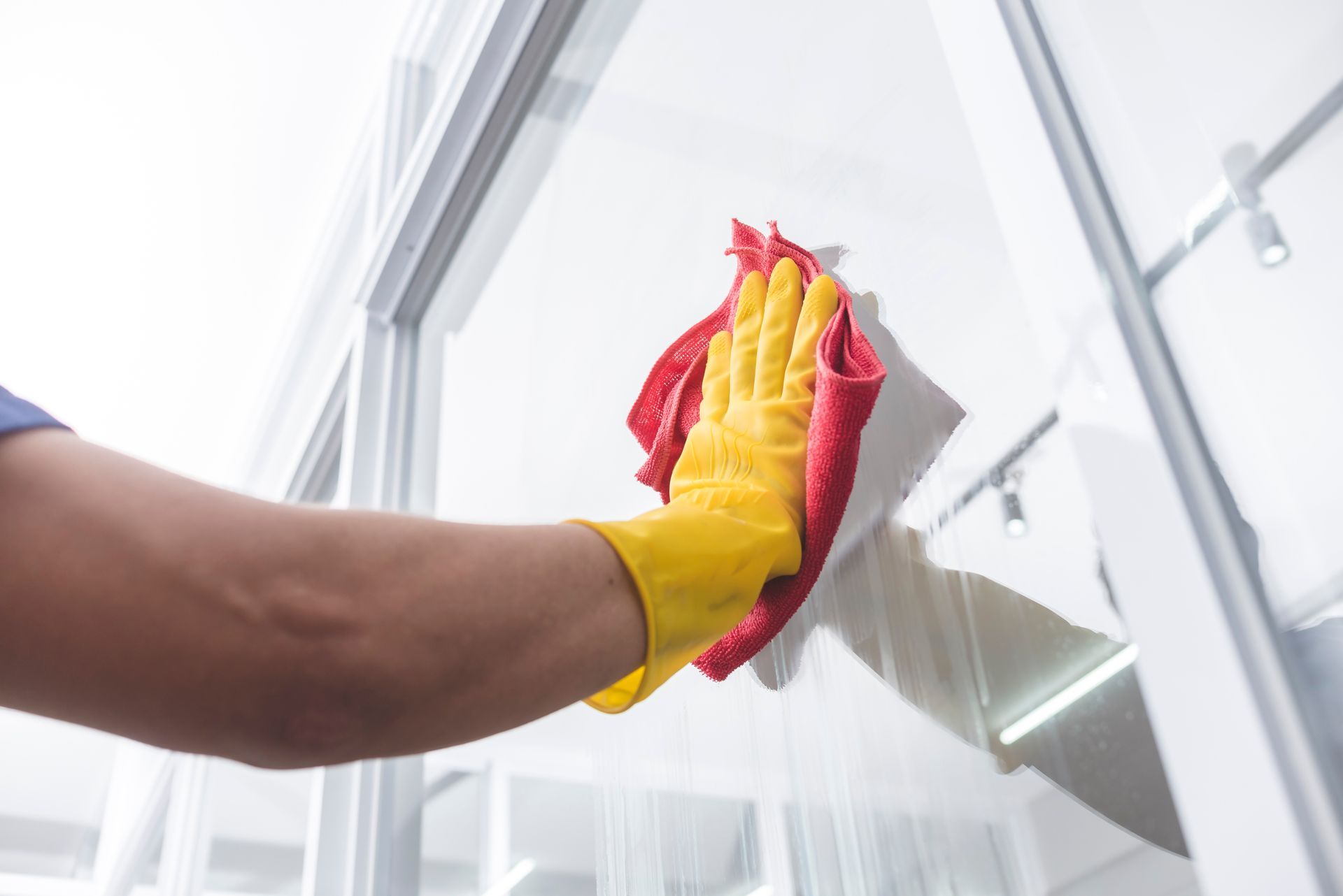 Hand in yellow glove wiping a glass window with a red cloth