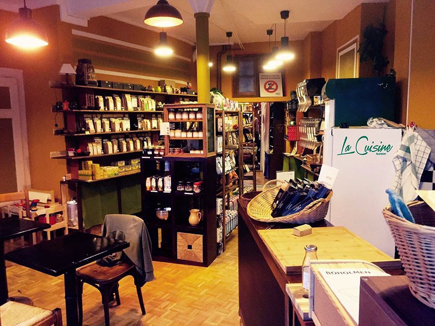 Intérieur d'une petite boutique avec des étagères, un comptoir et des tables. Éclairage chaleureux, murs jaunes.