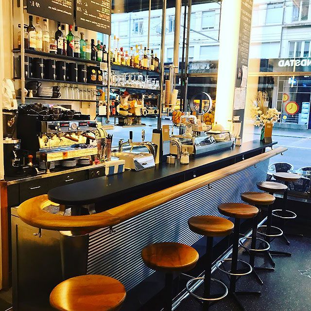 Bar à café avec tabourets, bouteilles d'alcool, machine à expresso et une fenêtre donnant sur une rue de la ville.
