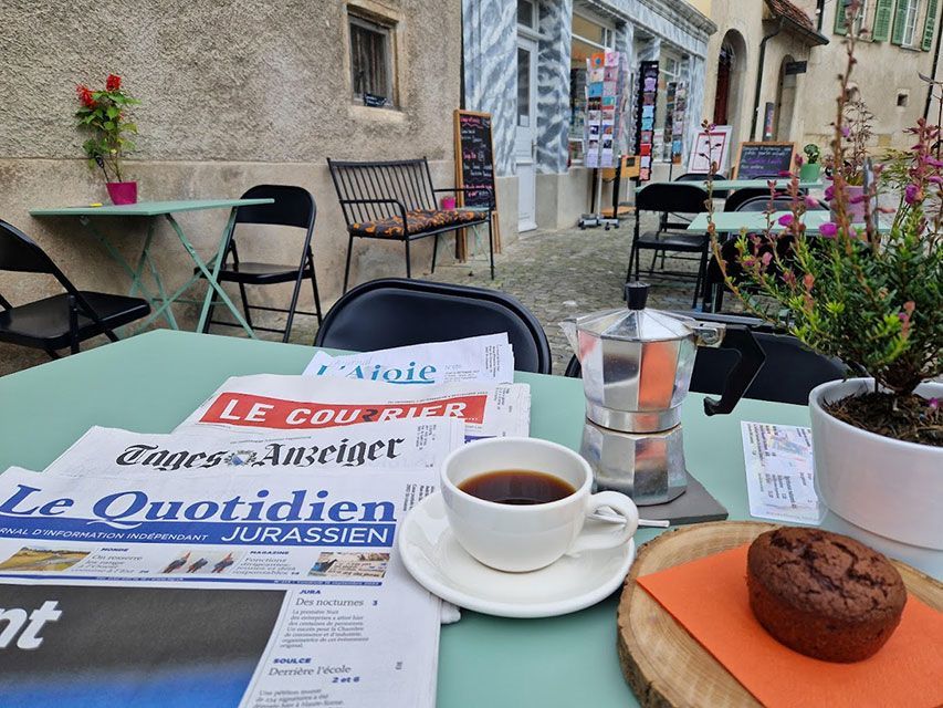 Café, journaux et muffins sur une table extérieure devant un magasin.