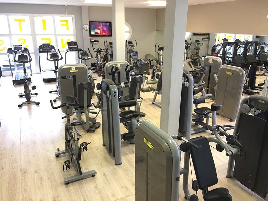 Salle de sport intérieure avec appareils d'exercice, notamment tapis roulants, vélos stationnaires et appareils de musculation.
