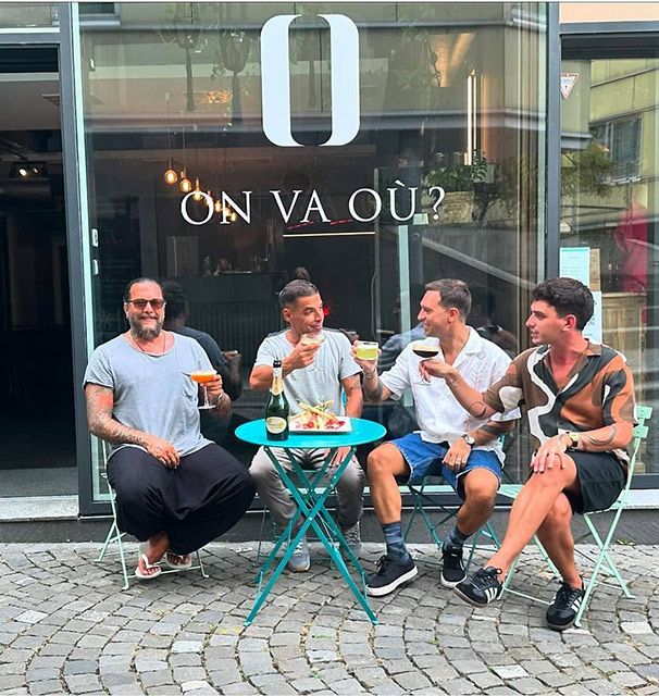 Quatre hommes trinquent à une table de bistrot devant un café.