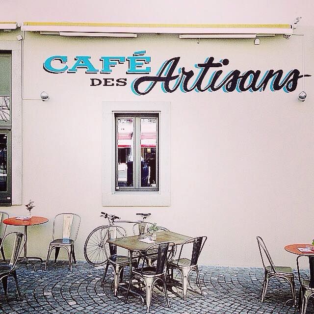Café des Artisans, avec des tables en extérieur, un vélo et une enseigne en écriture bleue.