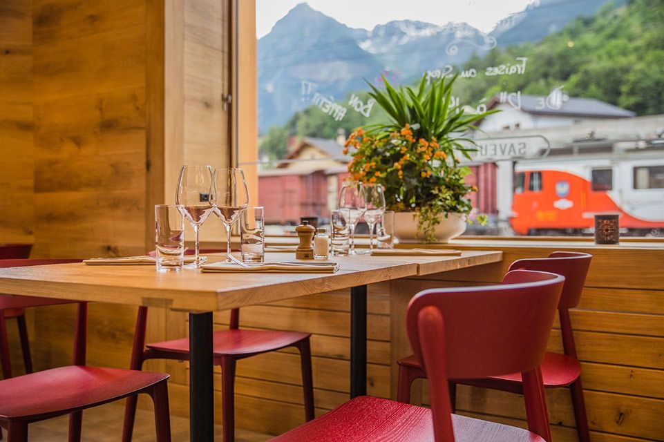 Ensemble de table de restaurant, chaises rouges, vue sur le train et les montagnes à travers la fenêtre.