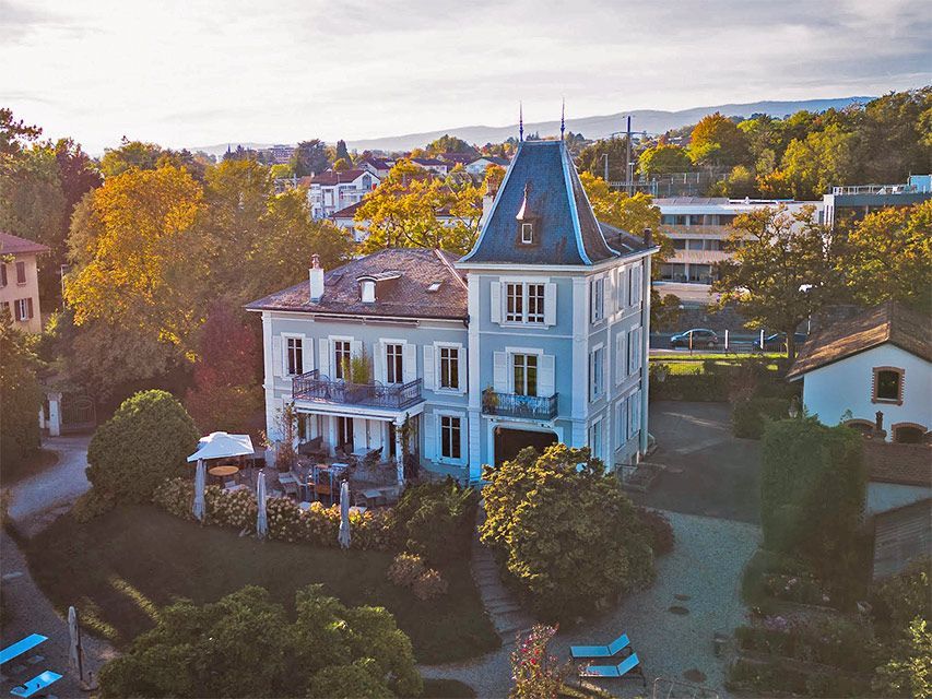 Élégant immeuble bleu clair à plusieurs étages avec une tour, entouré d'arbres, dans un quartier résidentiel.