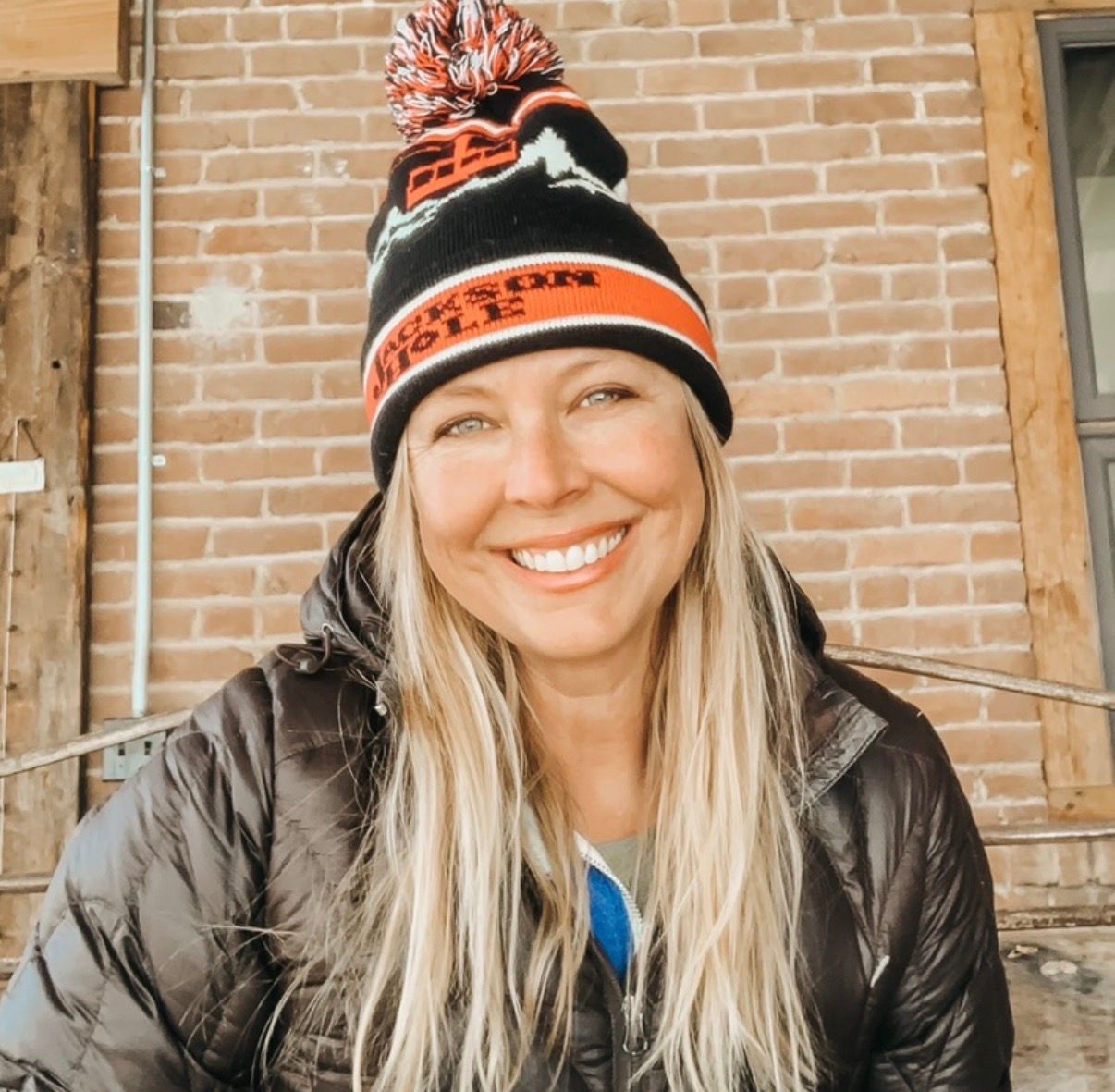 Yoga class outdoors on wooden walkway. Instructor in white top, black leggings; others in activewear. Trees in background.