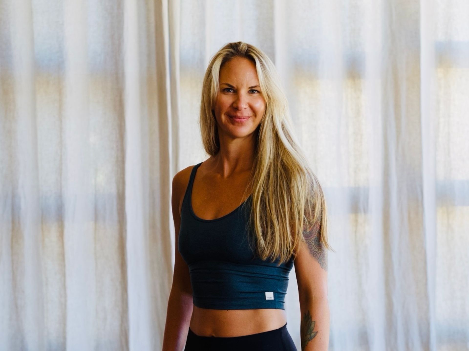 Man assisting woman in yoga pose, hands on back and shoulders; on a mat.