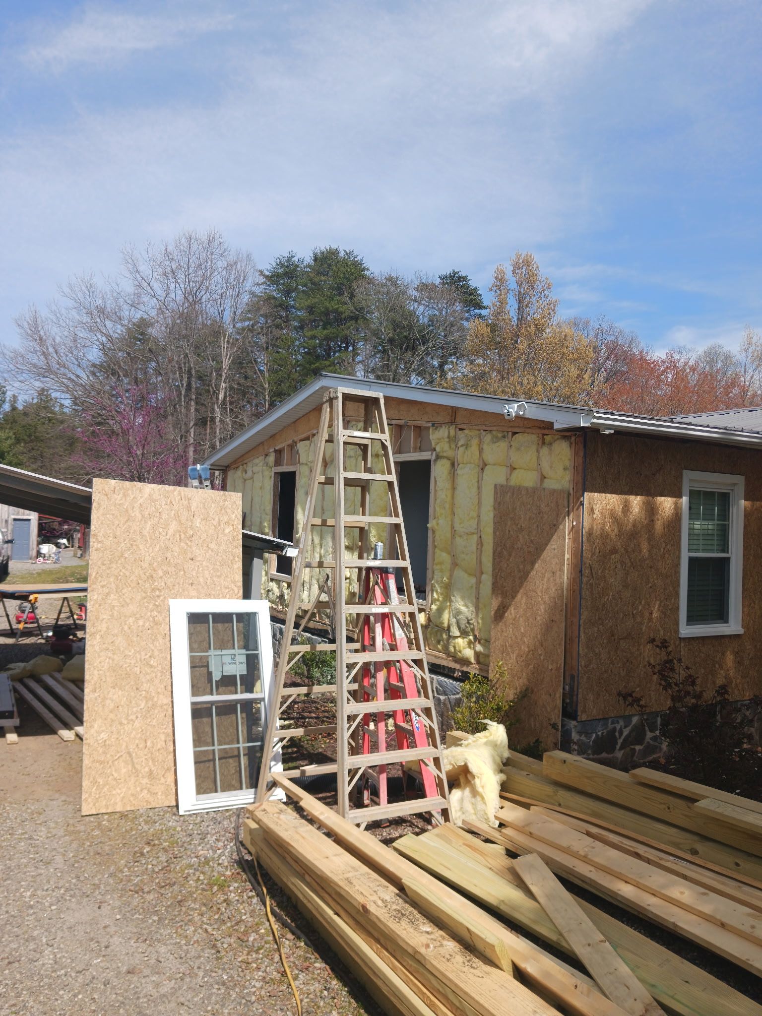 Building exterior under construction with exposed insulation, a ladder, and lumber.