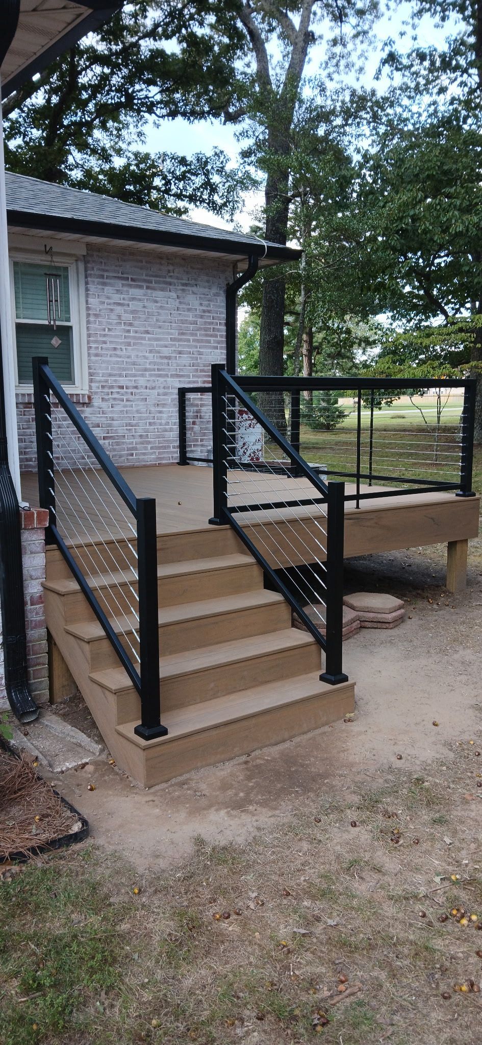 A wooden staircase with black railing leads up to a deck and the entrance of a building with stone siding.