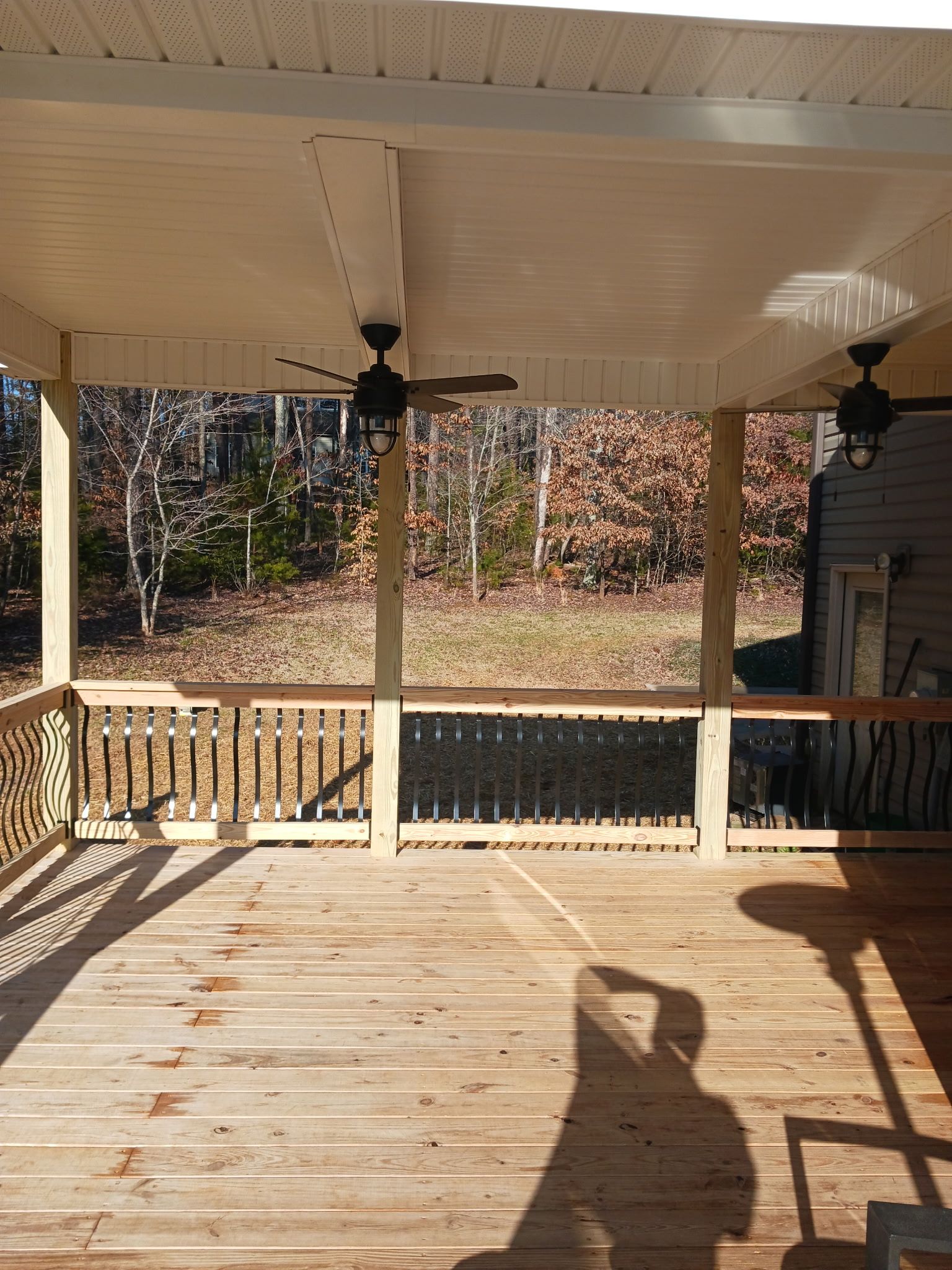 Wooden deck with a covered area, two ceiling fans, and a view of trees.