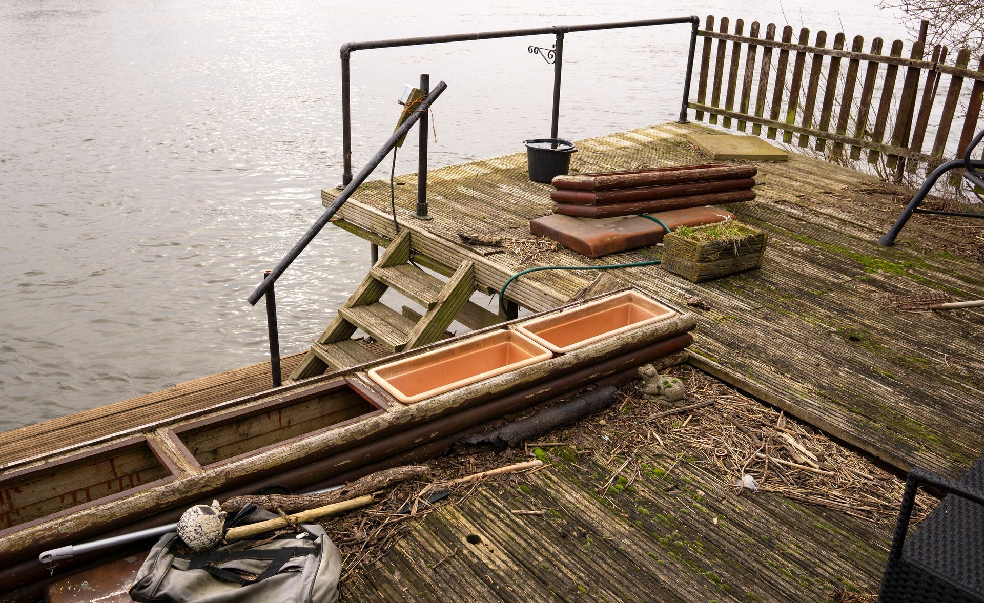 Wooden dock with steps leading into water, featuring railings, planters, and a small fence.