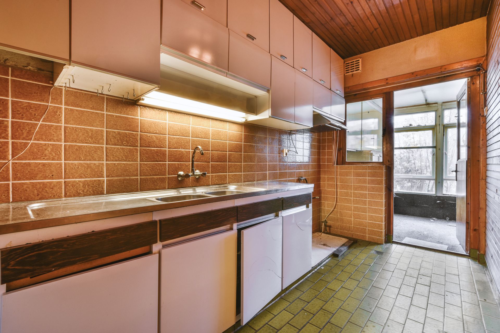 Small kitchen with brown tiled walls, white cabinets, and a doorway leading outside.