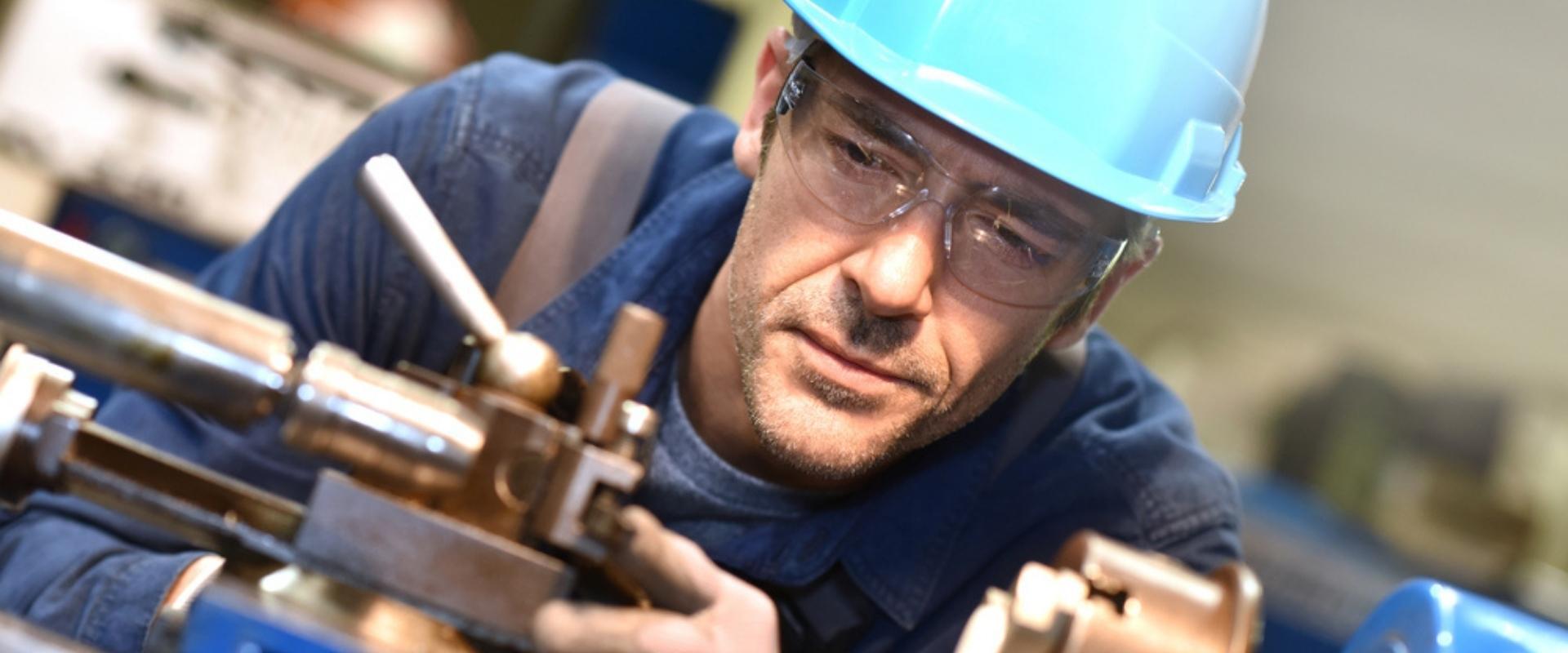 Ein Mann mit Schutzhelm und Schutzbrille arbeitet an einer Maschine.