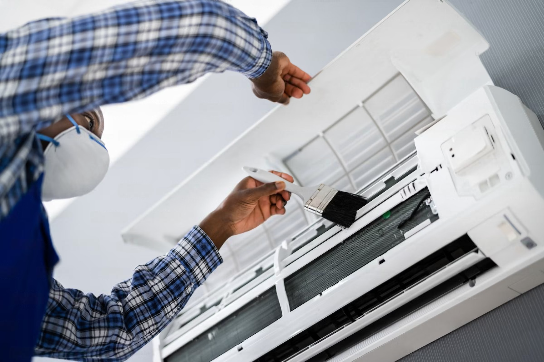 a man wearing a mask is cleaning an air conditioner with a brush