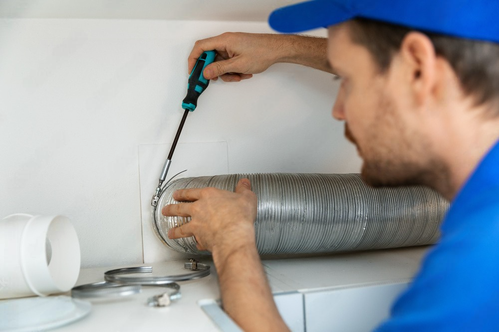 a man is fixing a ventilation pipe with a screwdriver .