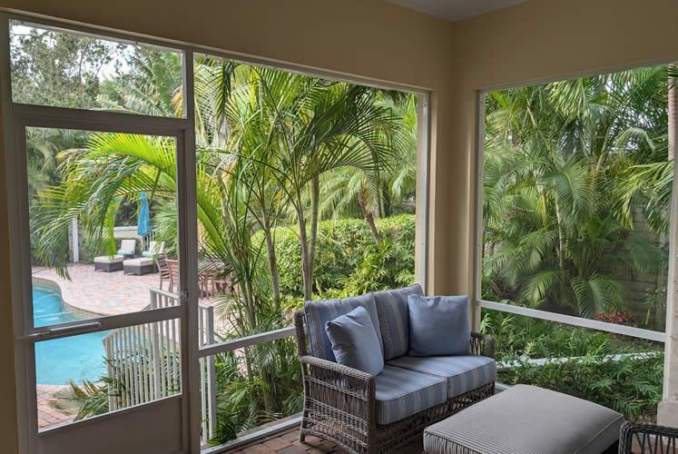 A screened in porch with a couch and ottoman and a view of a pool.