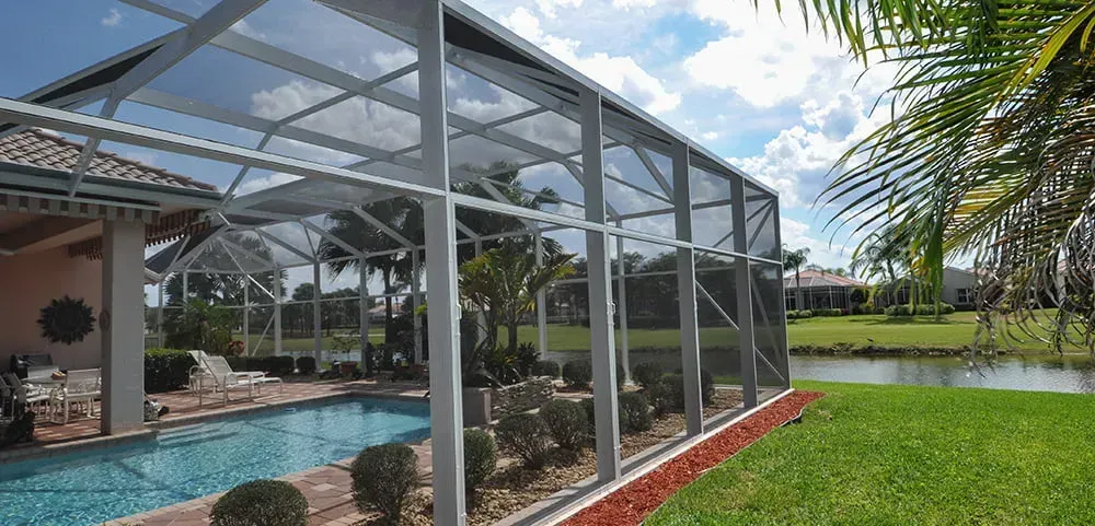 There is a swimming pool in the backyard of a house with a screened in area.