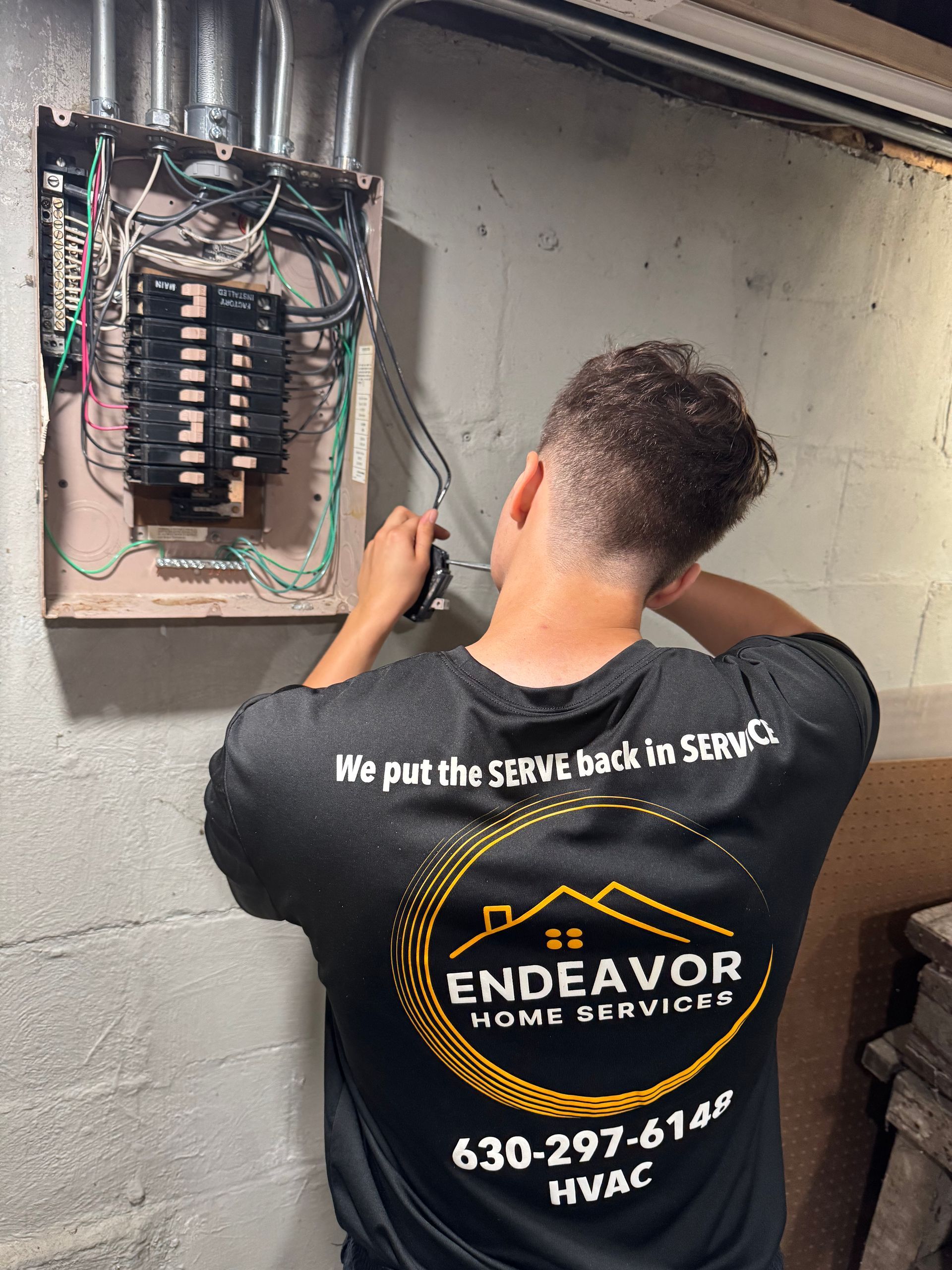 Electrician working on an electrical panel. He's wearing a black shirt with the company logo 