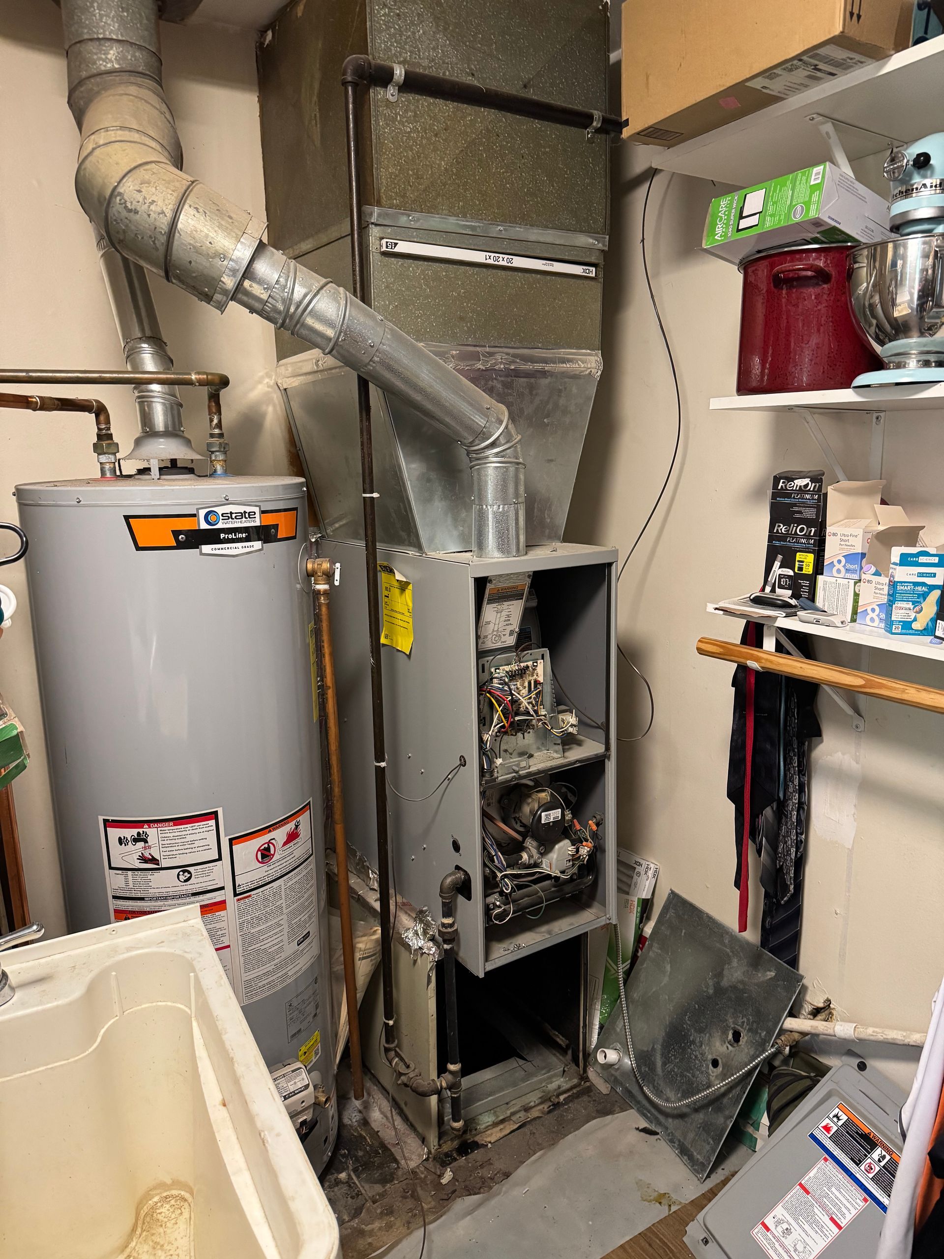 A utility room with a water heater, furnace, and laundry basin; various metal ductwork and shelves with items.