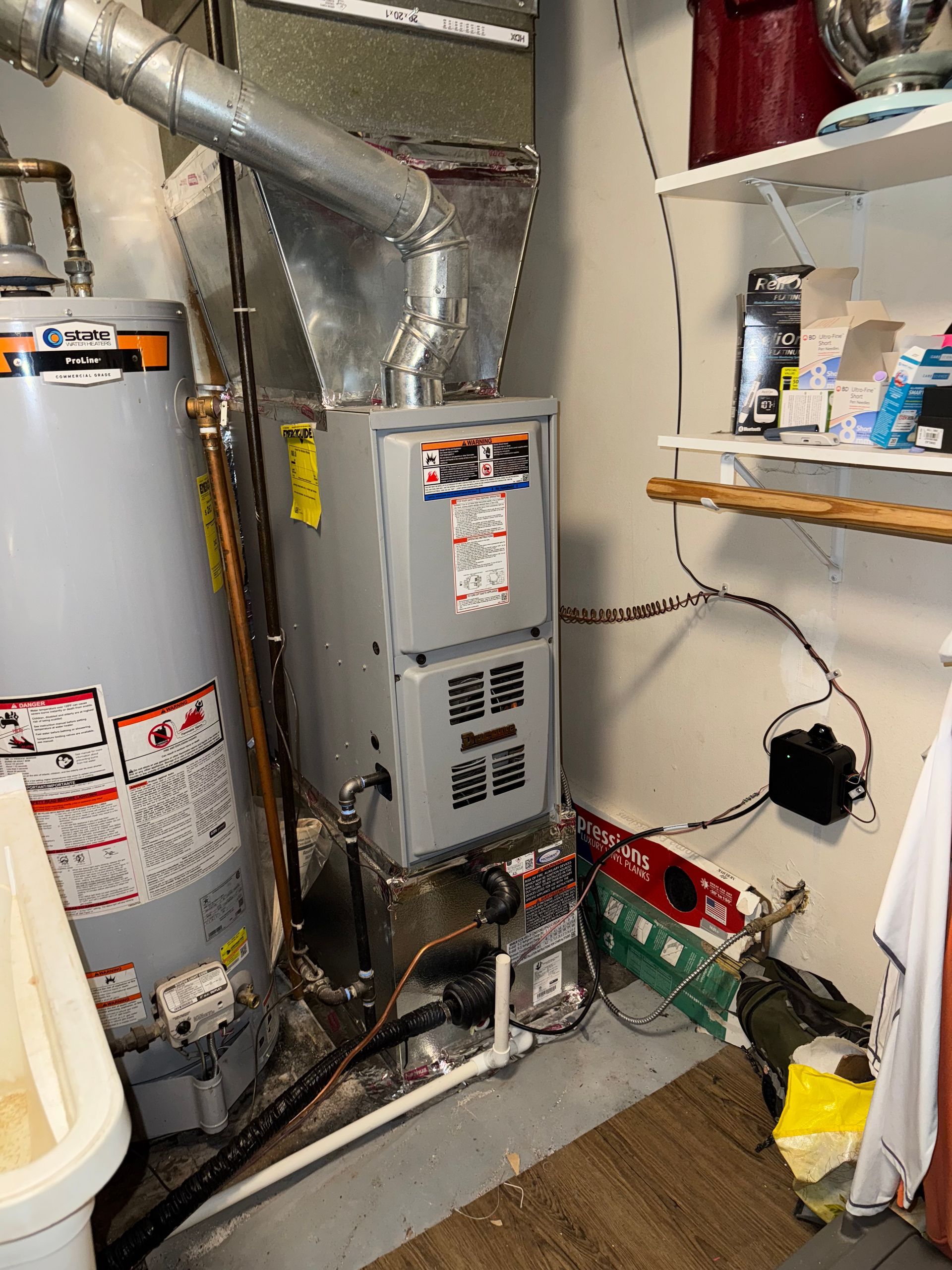 Furnace and water heater in a utility room. Ductwork, gas lines, and shelving are also present.