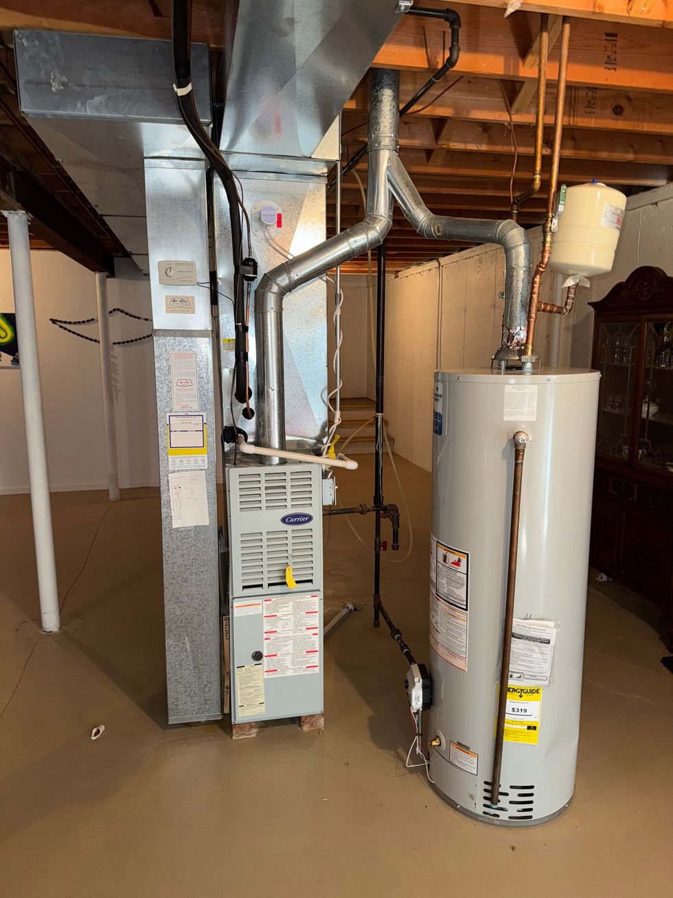 Furnace and water heater in a basement. Metal ducts and pipes are visible against white walls.