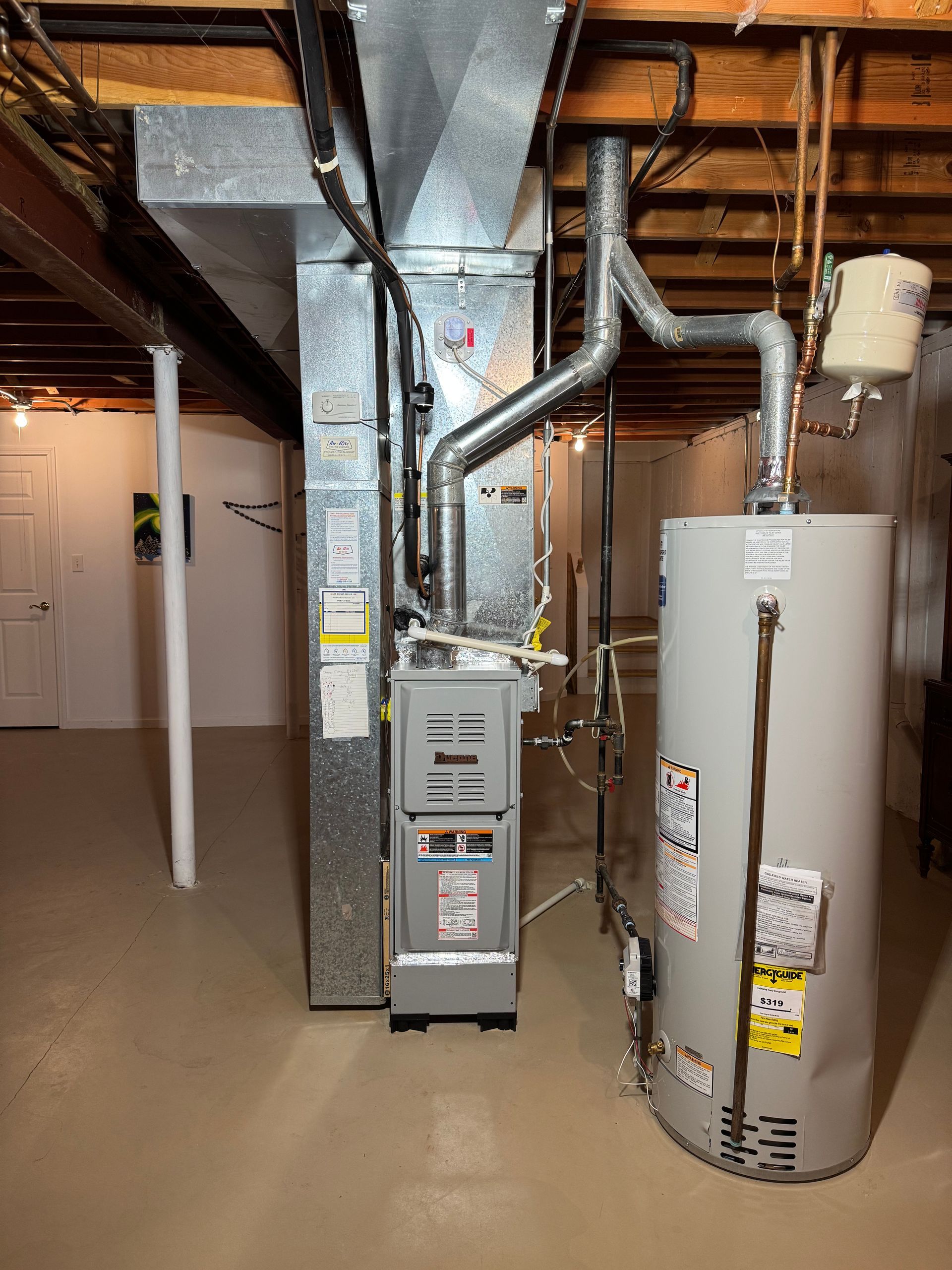 Furnace and water heater in a basement. Metal ducts and pipes are visible with beige floor and white walls.