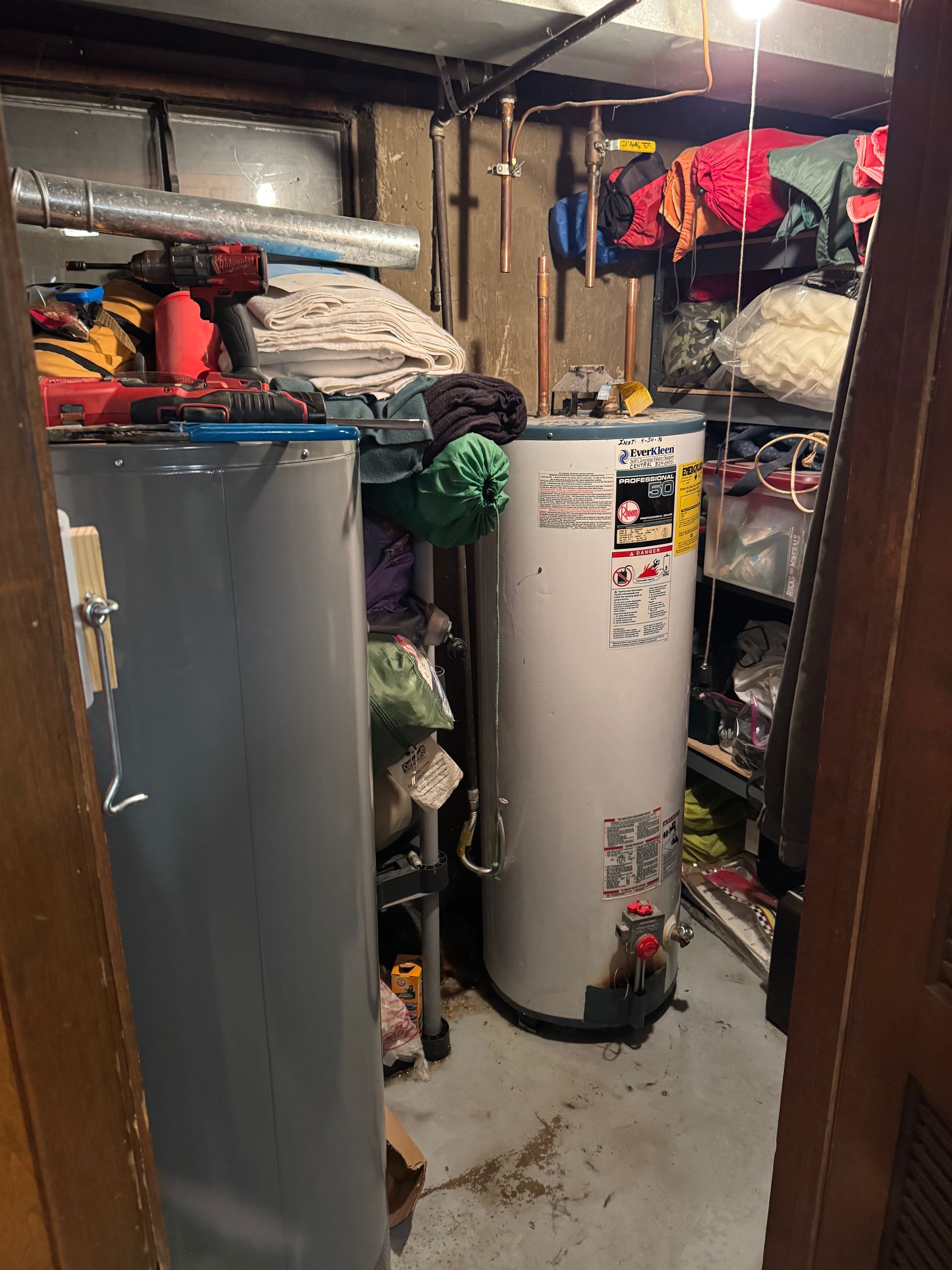 Cluttered basement with two water heaters, shelves, and storage.