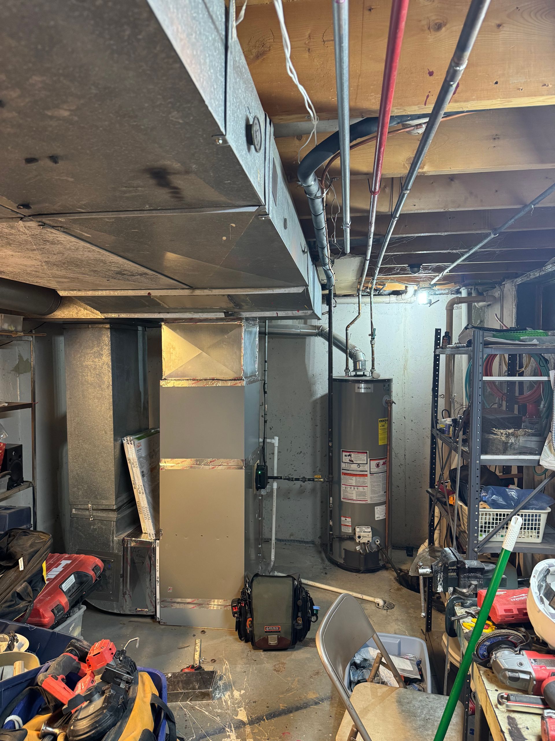 Basement with ductwork, water heater, and various tools on shelves. Exposed ceiling and concrete wall.