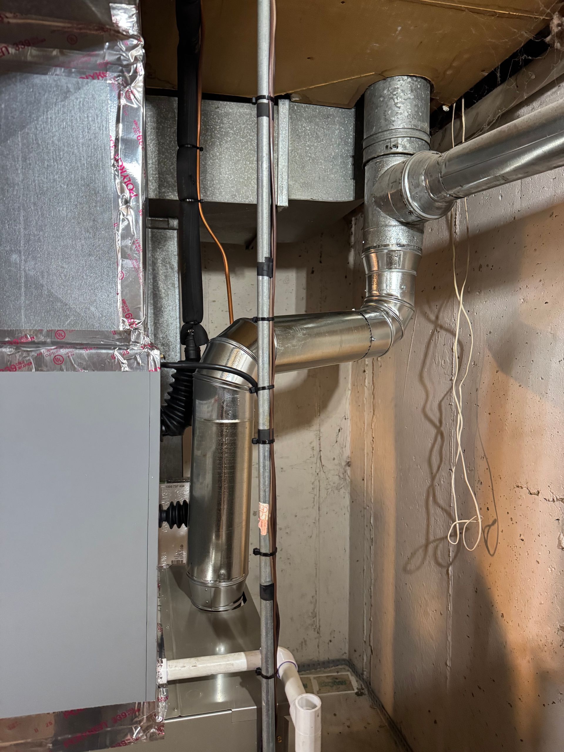 HVAC system components with ductwork and pipes in a basement corner.