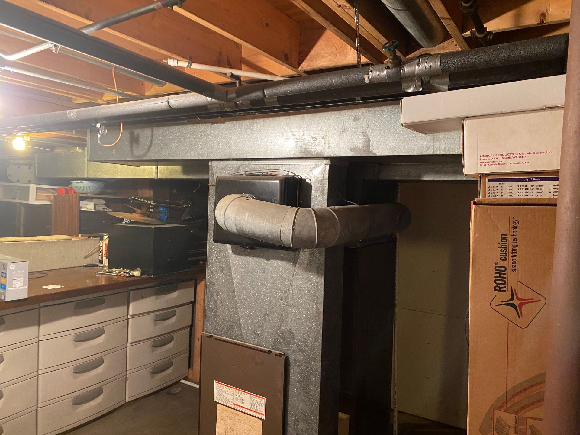 Basement with ductwork, boxes, and a workbench with drawers.