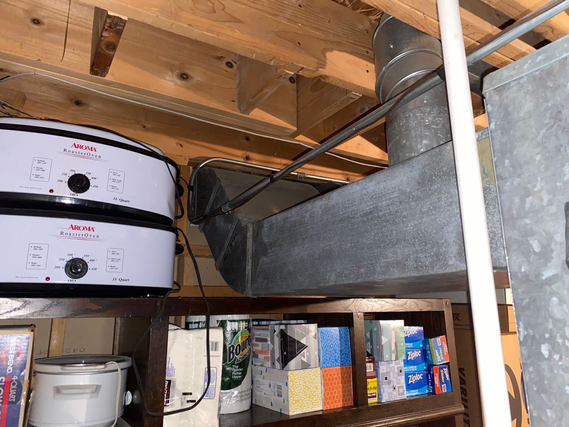 Kitchen appliances near a duct and shelves with goods.