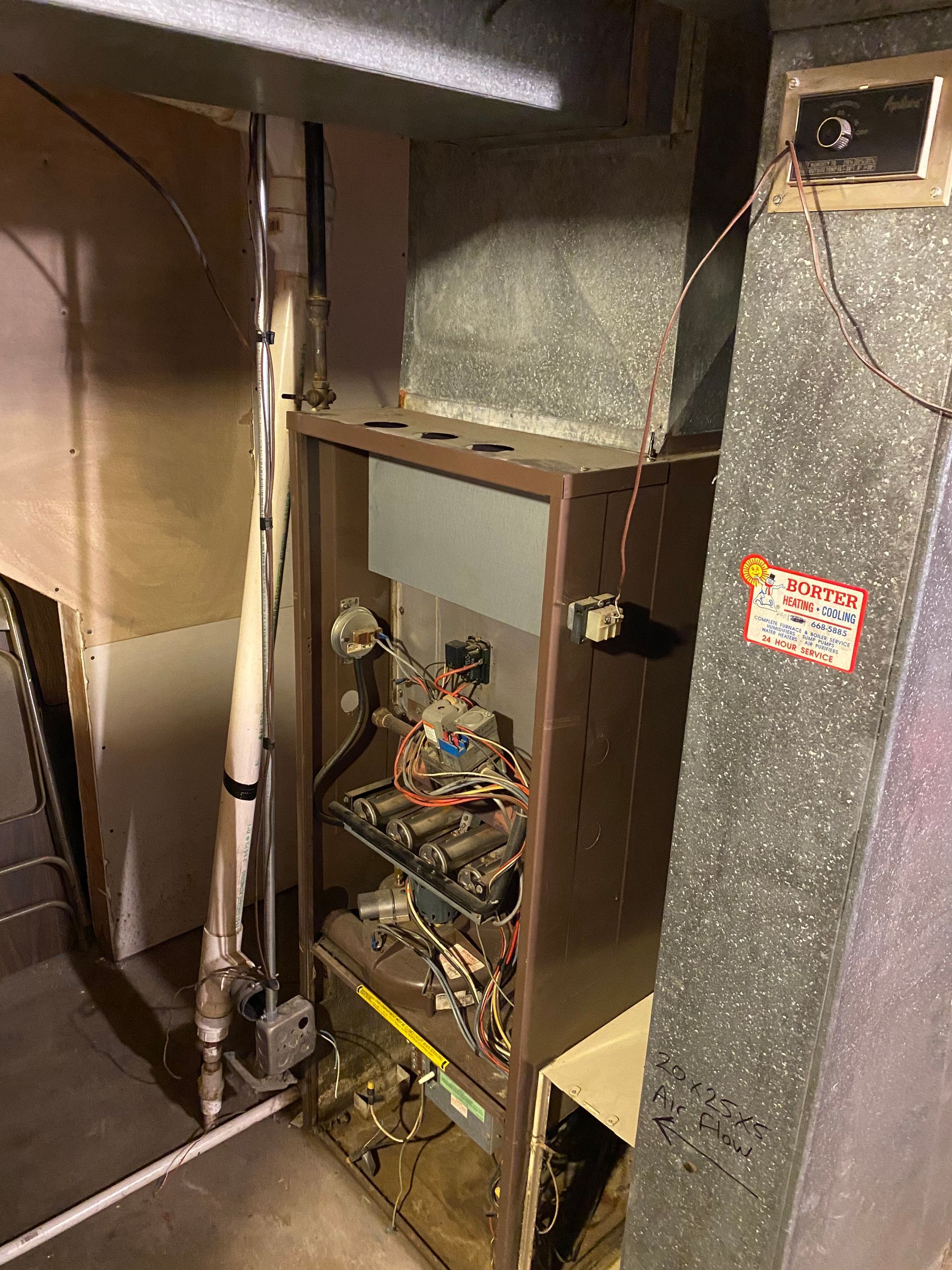 Furnace in a utility room; brown metal cabinet, ductwork, plumbing visible.