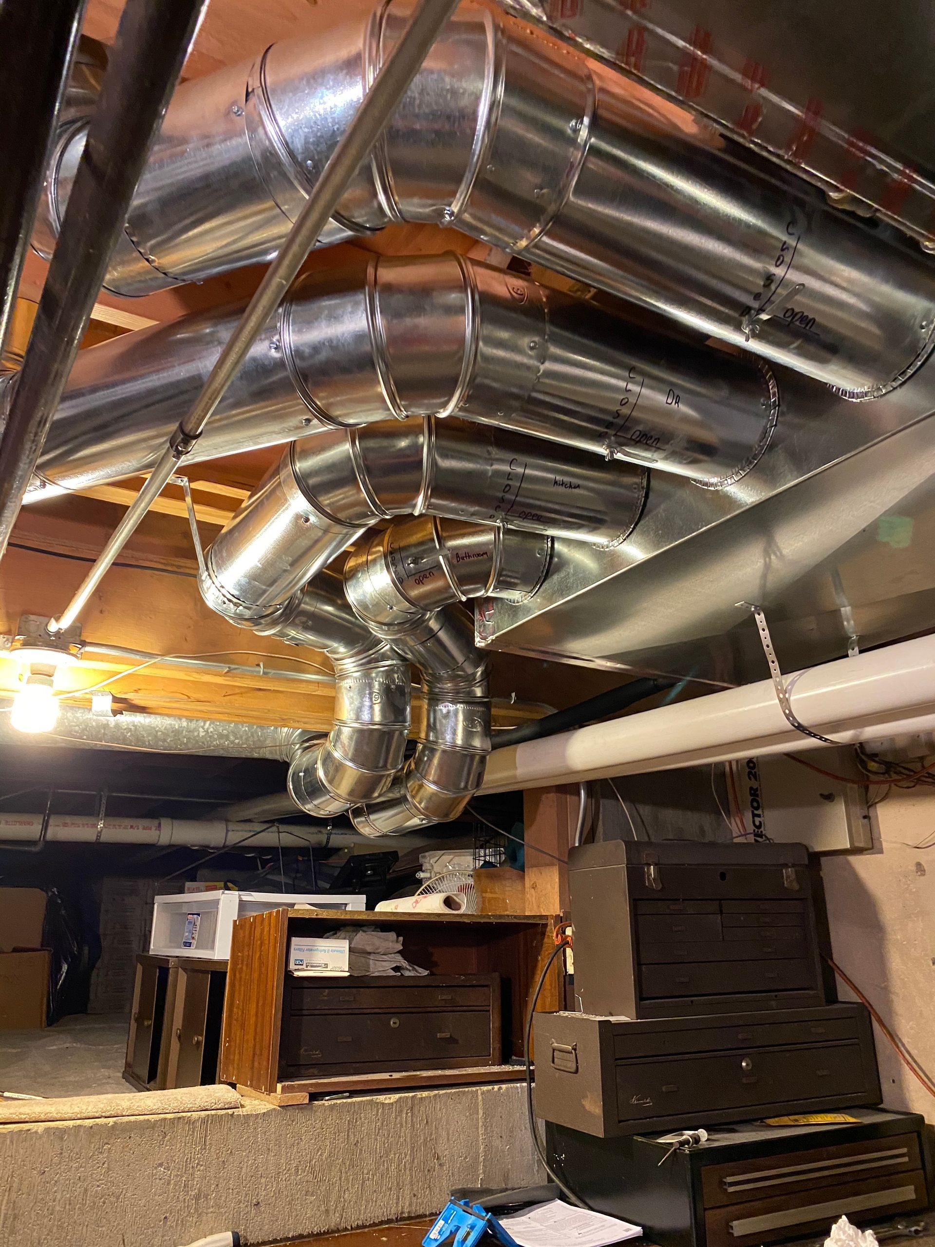 Silver HVAC ductwork installed in a basement ceiling, with wooden supports and a glimpse of storage below.