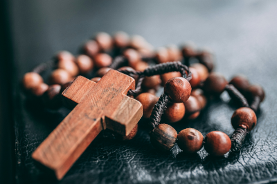 A wooden rosary with a cross on top of a bible.