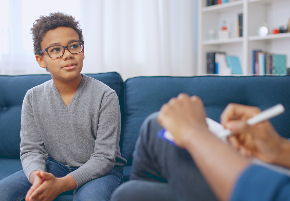 Um menino está sentado em um sofá conversando com um terapeuta.