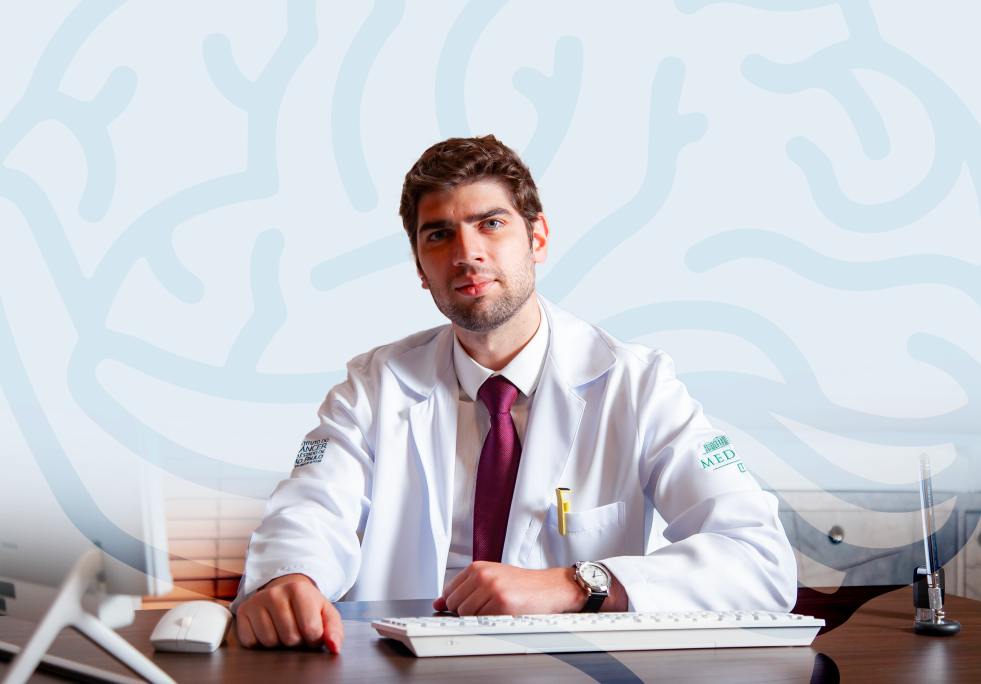 Um homem de jaleco e gravata está sentado em uma mesa.