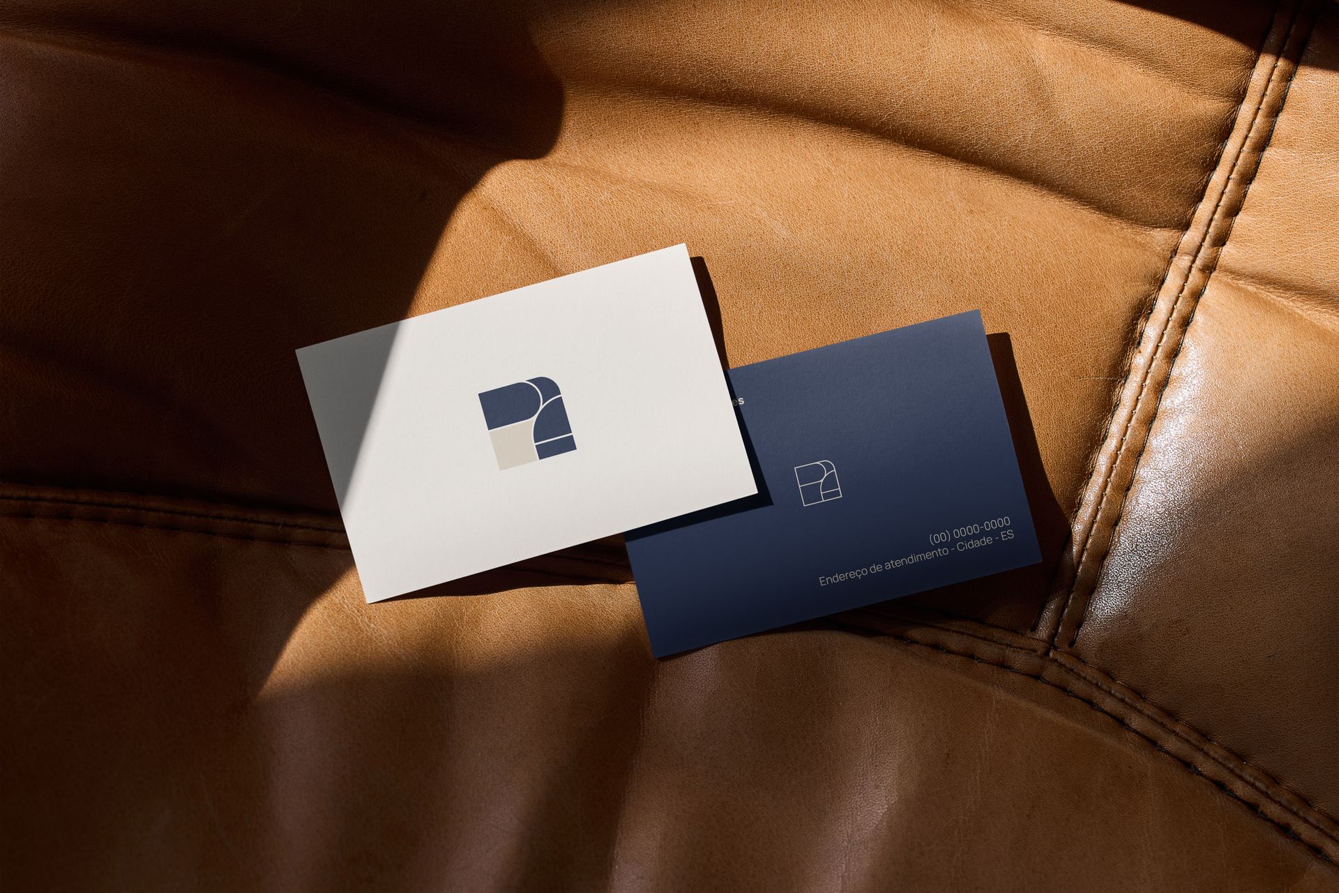 Dois cartões de visita em couro marrom; um branco com logotipo, um azul marinho com texto.
