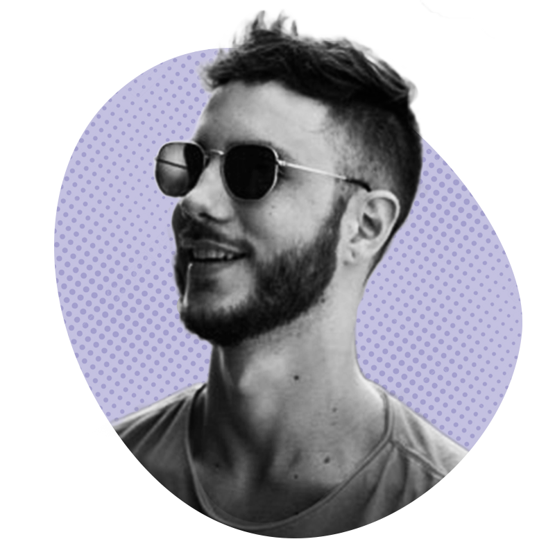 Homem de óculos escuros, barba curta e sorrindo, em frente a um fundo roxo pontilhado.